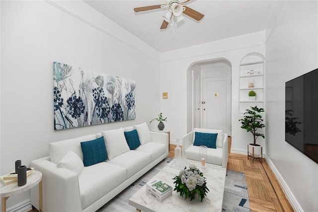 living room with built in features, baseboards, arched walkways, and ceiling fan