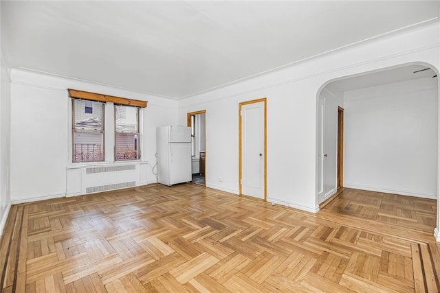 empty room featuring baseboards, arched walkways, and radiator