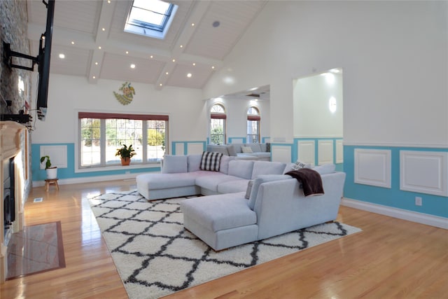 living area with light wood-type flooring, a wainscoted wall, high vaulted ceiling, recessed lighting, and a skylight