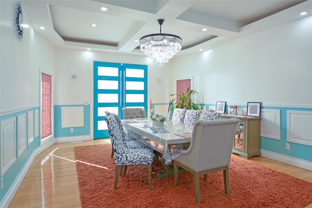 dining space with beamed ceiling, a notable chandelier, coffered ceiling, light wood-style floors, and a decorative wall