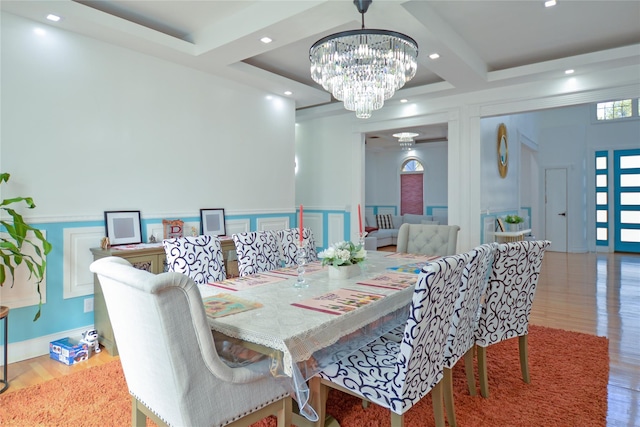 dining area featuring a decorative wall, beam ceiling, wood finished floors, a notable chandelier, and coffered ceiling