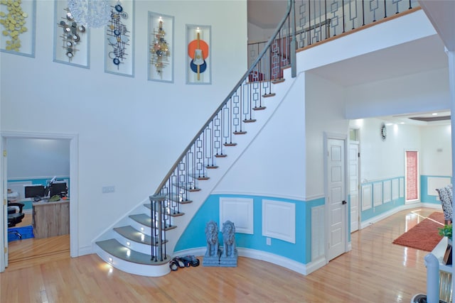 staircase featuring baseboards, wood finished floors, and a towering ceiling