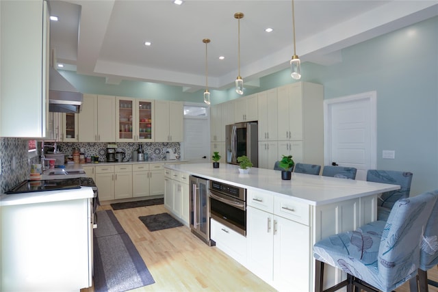 kitchen featuring a tray ceiling, light wood-style flooring, decorative backsplash, wine cooler, and appliances with stainless steel finishes