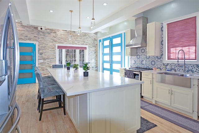 kitchen with a wealth of natural light, stainless steel refrigerator, a sink, backsplash, and wall chimney exhaust hood