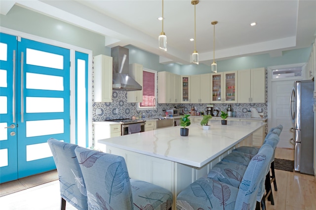 kitchen featuring light wood finished floors, decorative backsplash, appliances with stainless steel finishes, wall chimney range hood, and a center island