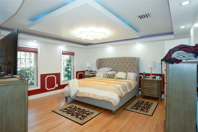 bedroom featuring visible vents, a raised ceiling, baseboards, and wood finished floors