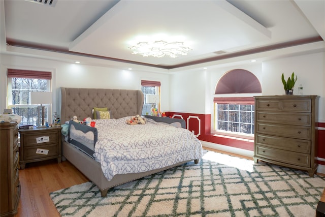 bedroom with a tray ceiling, light wood-style flooring, and visible vents