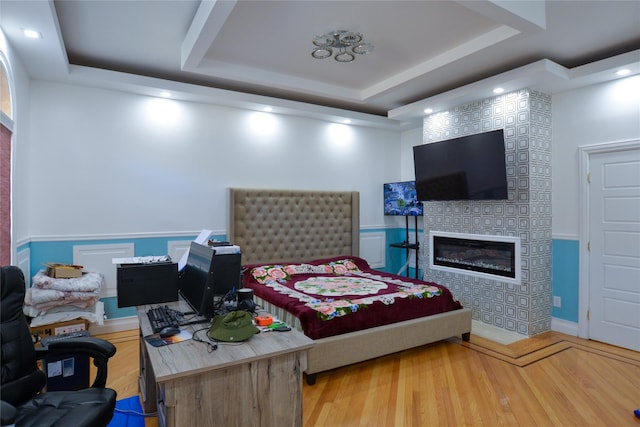 bedroom featuring a fireplace, a raised ceiling, and light wood-style floors