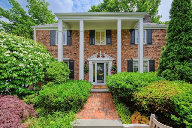 greek revival house featuring brick siding and a chimney