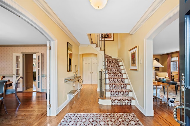 interior space with wallpapered walls, crown molding, stairway, and wood finished floors