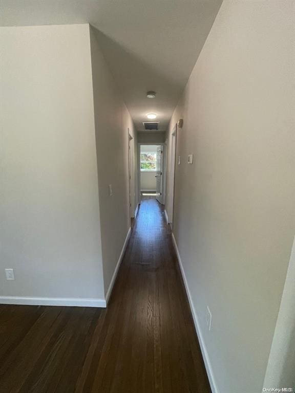 hallway featuring visible vents, baseboards, and dark wood-style flooring