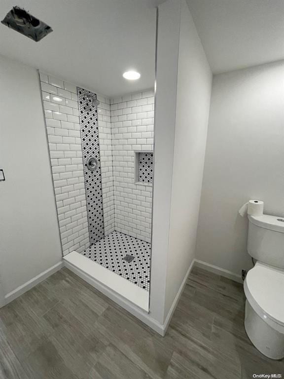 full bathroom featuring a tile shower, toilet, baseboards, and wood finished floors