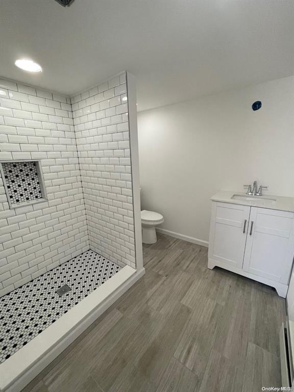 bathroom featuring vanity, wood finished floors, baseboards, tiled shower, and toilet