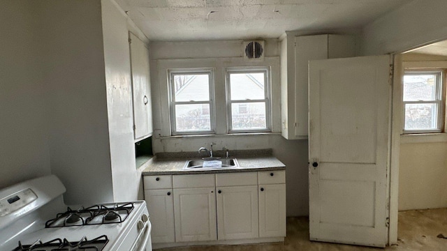 kitchen with a sink, white gas range, white cabinets, and light countertops