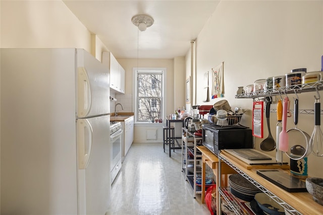 kitchen with white appliances, white cabinets, tasteful backsplash, and a sink