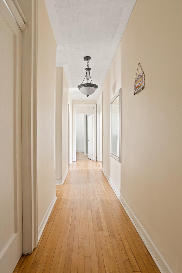 hall featuring baseboards, light wood finished floors, and a textured ceiling