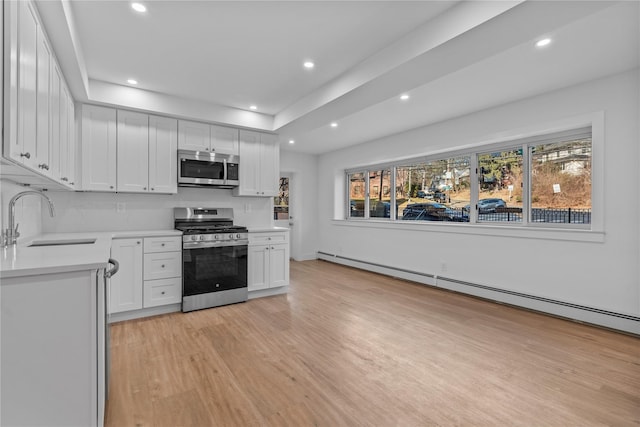 kitchen featuring a sink, stainless steel appliances, light wood finished floors, baseboard heating, and light countertops