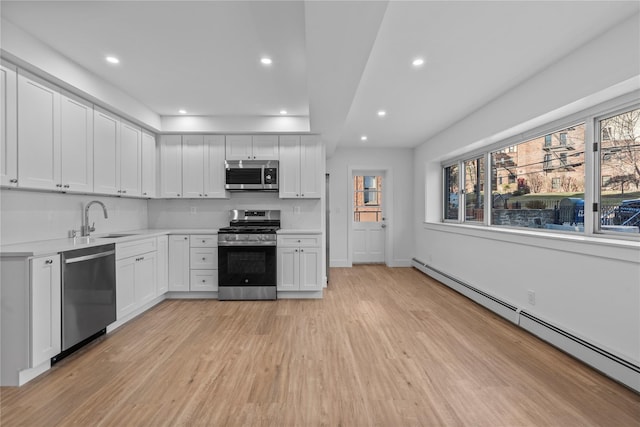 kitchen featuring a baseboard heating unit, light wood-type flooring, light countertops, appliances with stainless steel finishes, and a sink