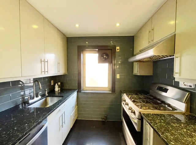 kitchen with under cabinet range hood, stainless steel appliances, dark stone countertops, and a sink