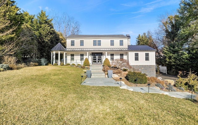 view of front of house with a standing seam roof, a front yard, covered porch, and stone siding