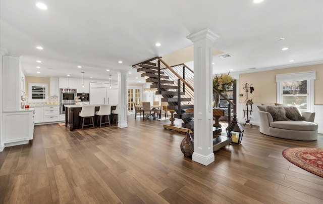 living area featuring crown molding, decorative columns, dark wood-style floors, and visible vents