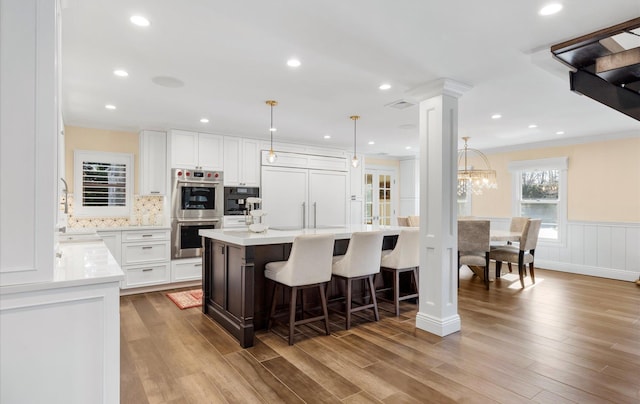 kitchen featuring paneled refrigerator, stainless steel double oven, a breakfast bar area, light countertops, and ornate columns