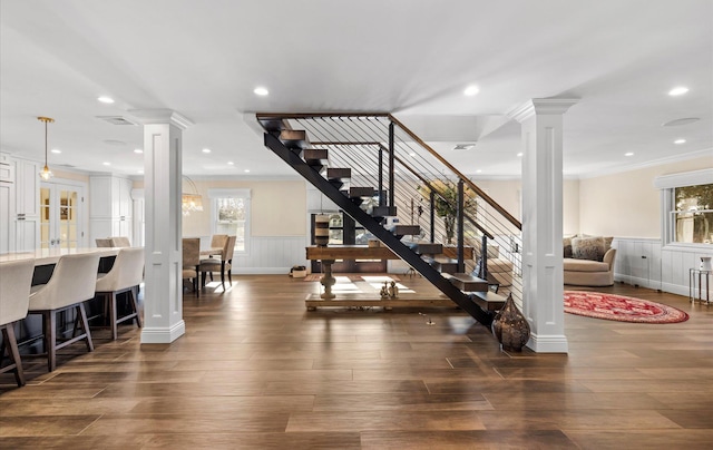 stairway featuring decorative columns, wood finished floors, a wainscoted wall, and ornamental molding