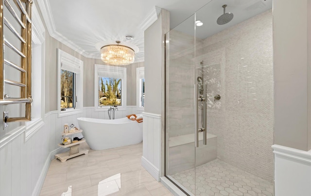 bathroom with ornamental molding, an inviting chandelier, wainscoting, a shower stall, and a soaking tub