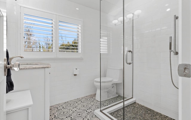 bathroom featuring tile patterned flooring, toilet, vanity, a stall shower, and tile walls