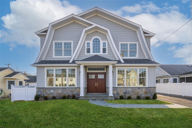 shingle-style home featuring stone siding, a front lawn, and fence