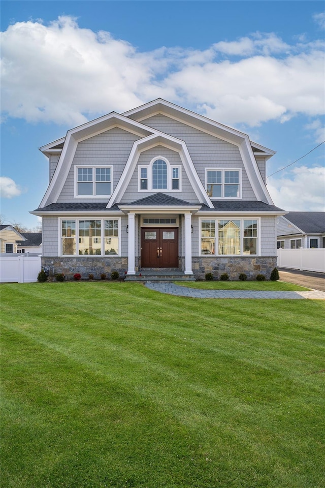 shingle-style home with a front lawn, fence, and stone siding