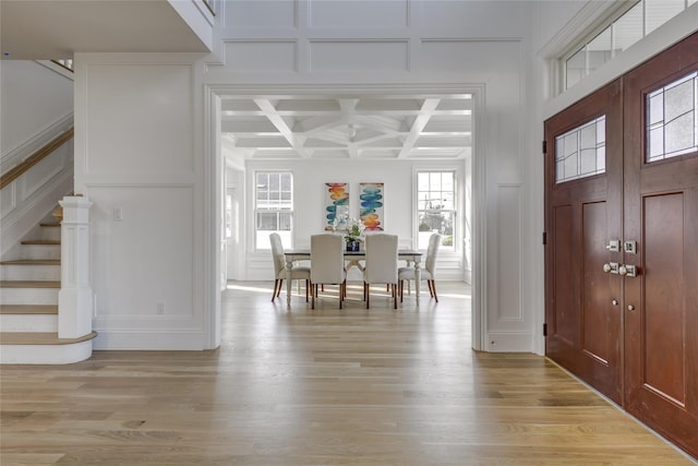 entrance foyer featuring light wood-style floors, coffered ceiling, stairs, and a decorative wall