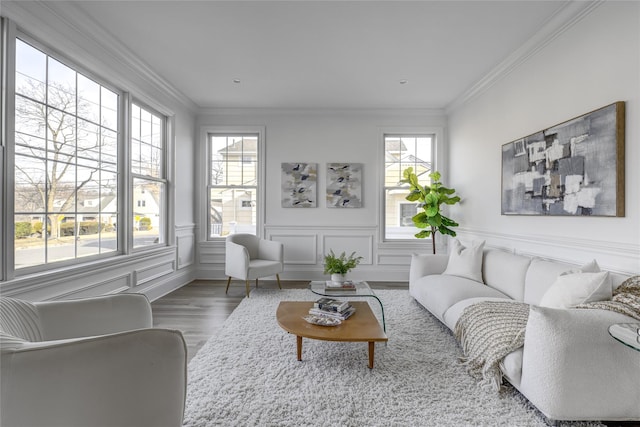 living area with wood finished floors, ornamental molding, wainscoting, and a decorative wall