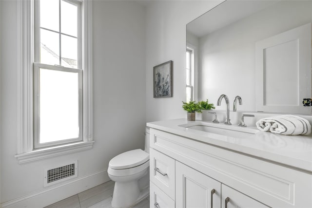 bathroom featuring toilet, plenty of natural light, vanity, and visible vents