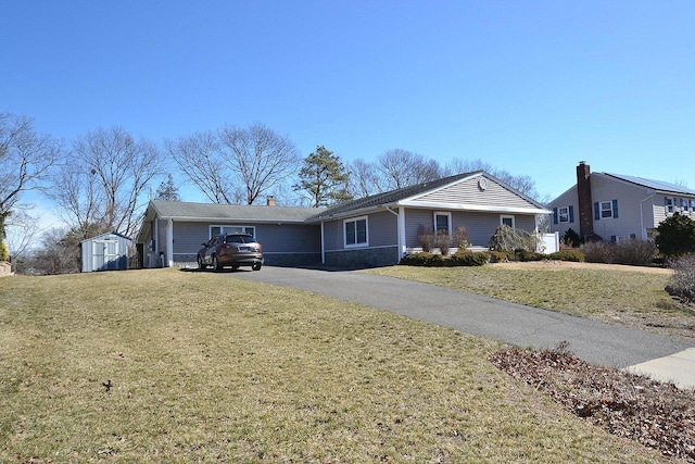 single story home with aphalt driveway, a storage unit, a front lawn, and an outdoor structure