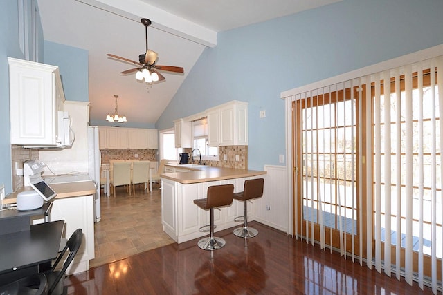 kitchen with white appliances, dark wood-style floors, a peninsula, a sink, and beamed ceiling