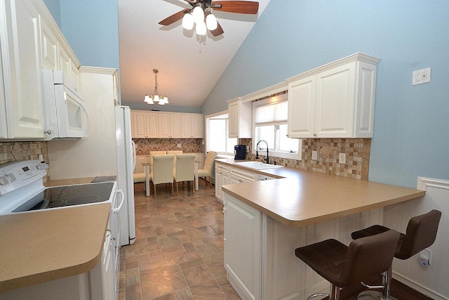 kitchen featuring light countertops, a kitchen bar, a peninsula, white appliances, and a sink