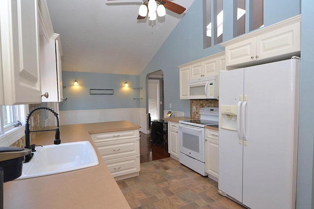 kitchen with a sink, white appliances, arched walkways, and white cabinetry