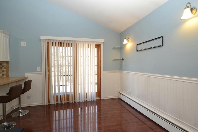 dining space featuring a wainscoted wall, lofted ceiling, baseboard heating, and wood finished floors