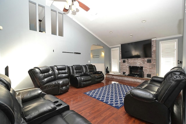 living room featuring wood finished floors, arched walkways, crown molding, a brick fireplace, and vaulted ceiling