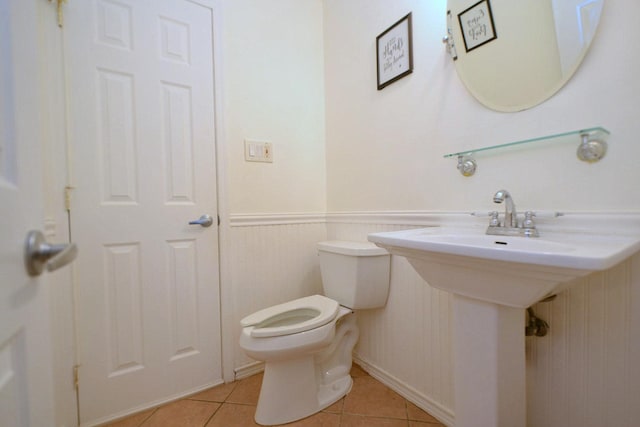 bathroom with tile patterned floors, toilet, and a wainscoted wall