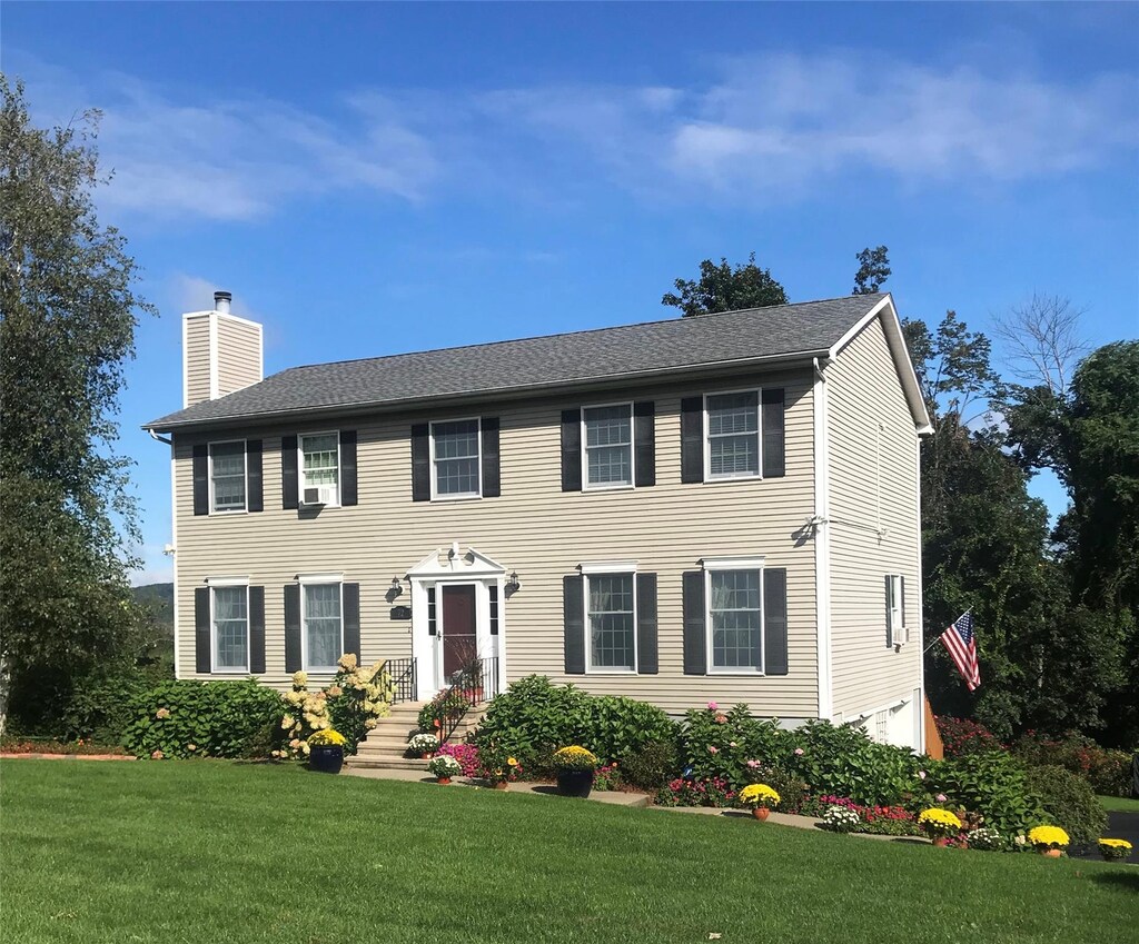 colonial house featuring a front yard, roof with shingles, and a chimney