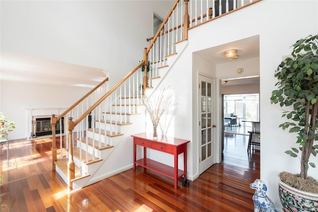 stairway with a high ceiling, baseboards, wood-type flooring, and a premium fireplace