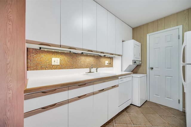 kitchen with backsplash, white cabinets, white appliances, stacked washer / drying machine, and a sink