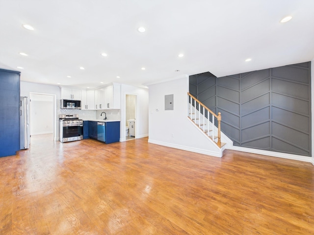 unfurnished living room featuring stairs, electric panel, recessed lighting, light wood-style floors, and a sink