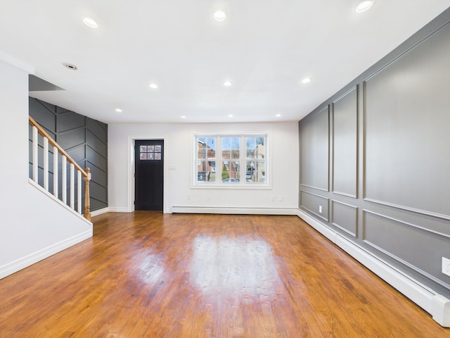 entryway with stairway, a decorative wall, wood finished floors, and a baseboard radiator