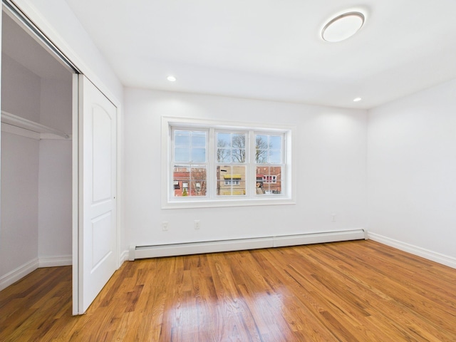 unfurnished bedroom featuring wood finished floors, recessed lighting, a closet, a baseboard radiator, and baseboards