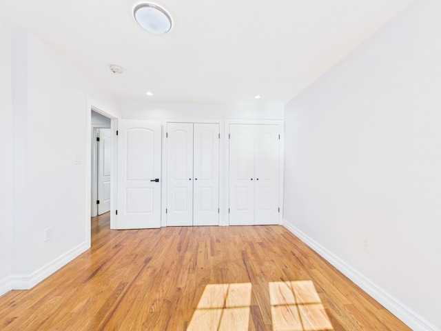 unfurnished bedroom featuring baseboards, recessed lighting, two closets, and light wood-style floors