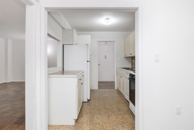 kitchen with freestanding refrigerator, a sink, light countertops, white cabinetry, and range