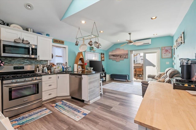 kitchen with lofted ceiling, a peninsula, a sink, appliances with stainless steel finishes, and open floor plan